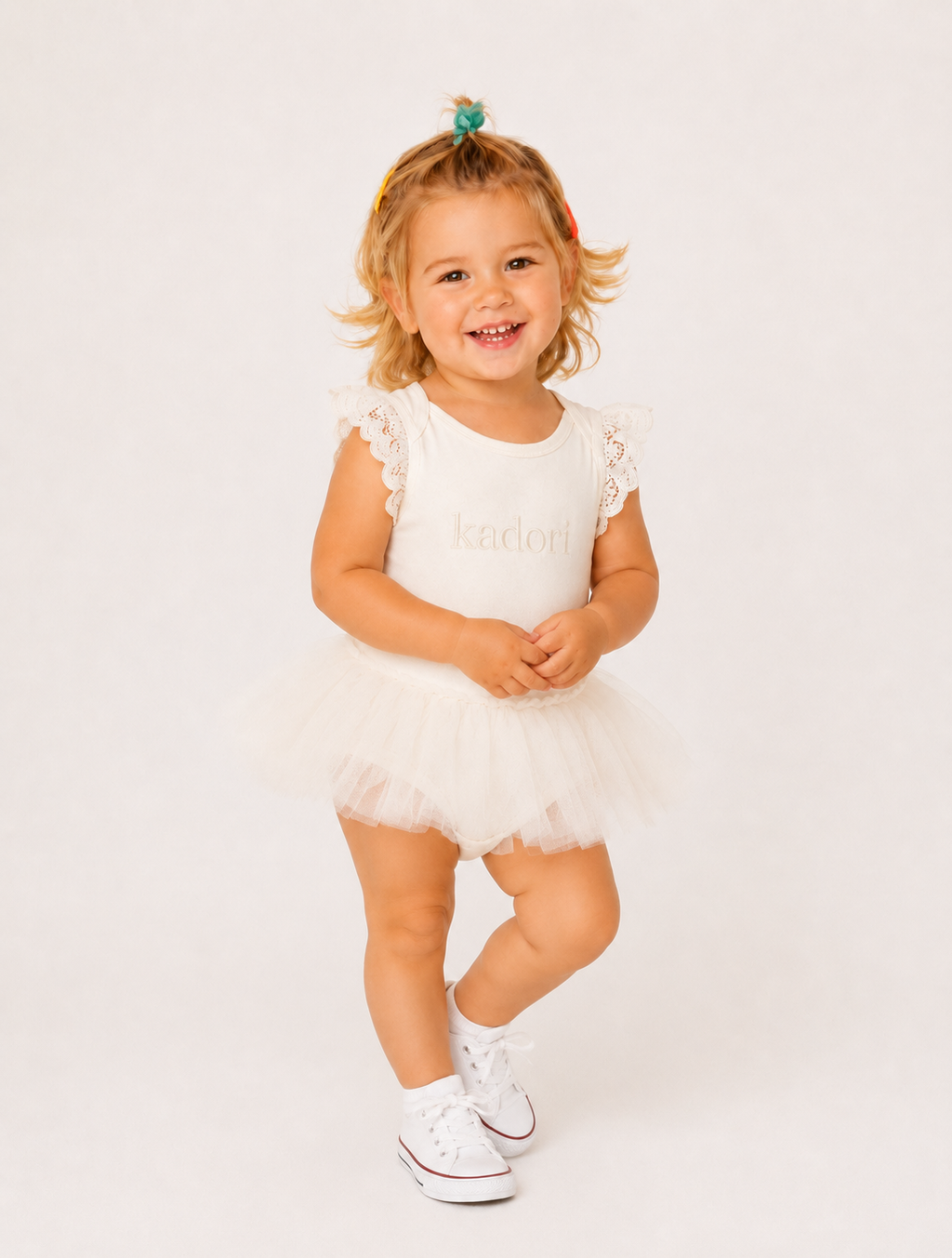 A toddler girl wearing a white tutu dress with lace flutter sleeves and the name 'Evelyn' printed on the chest, standing against a plain white studio background.
