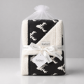 A folded baby blanket with a black and white reindeer pattern, wrapped in a clear cellophane bag and tied with a white ribbon printed with the brand name 'kadorf'.