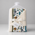 A folded baby blanket with a woodland bear and tree pattern, wrapped in a clear plastic bag and tied with a white ribbon printed with the brand name 'kadori'.