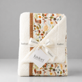 A folded Kadori baby blanket with a cream sherpa border and a multicolor autumn-themed patchwork pattern, tied with a white ribbon and tag.
