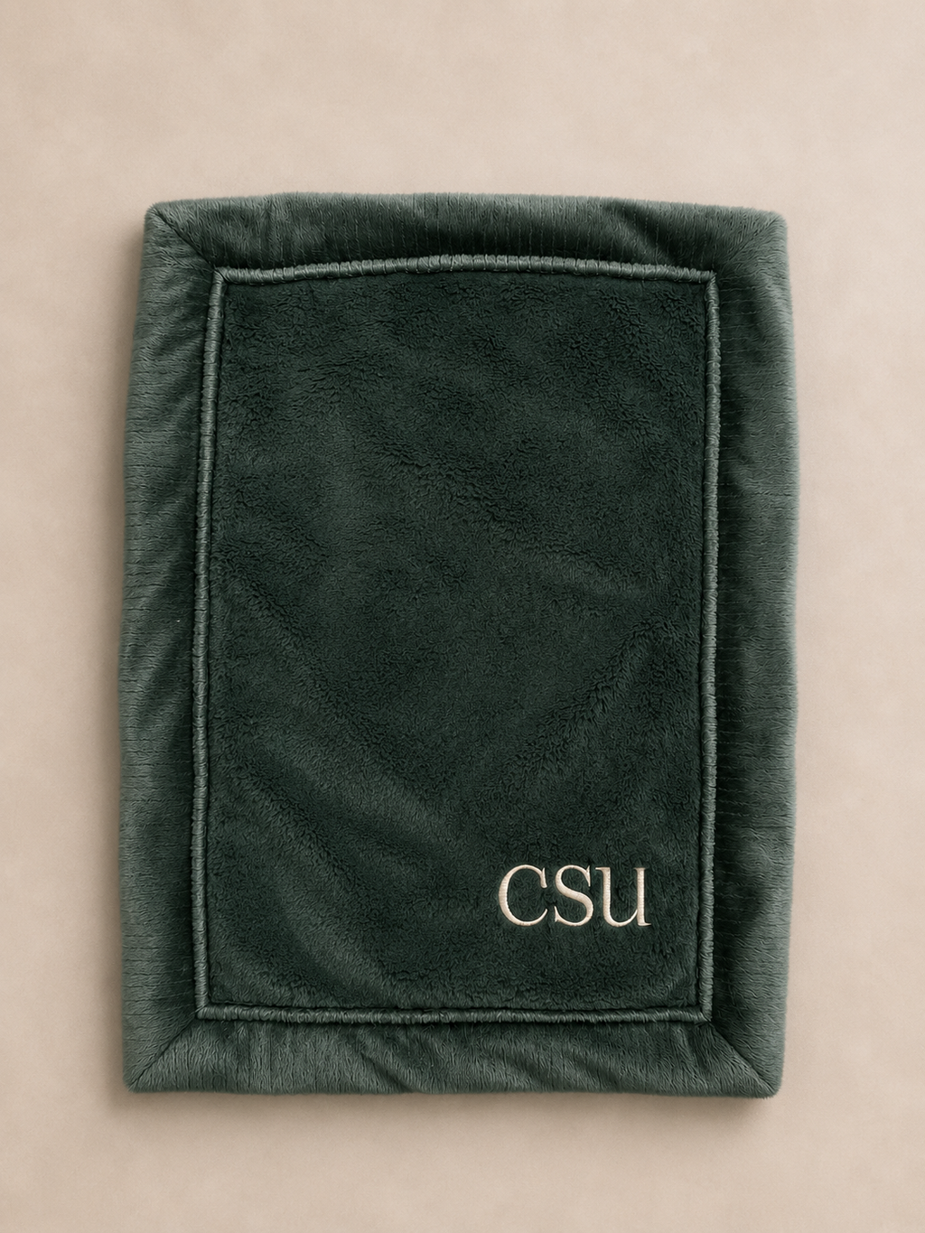 A dark green plush fleece blanket with a stitched border and the letters 'CSU' embroidered in gold at the bottom right, shown flat on a light beige background.