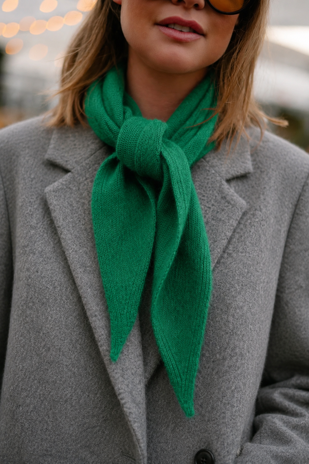 A bright green knit scarf tied in a knot and worn around the neck, styled with a gray coat.