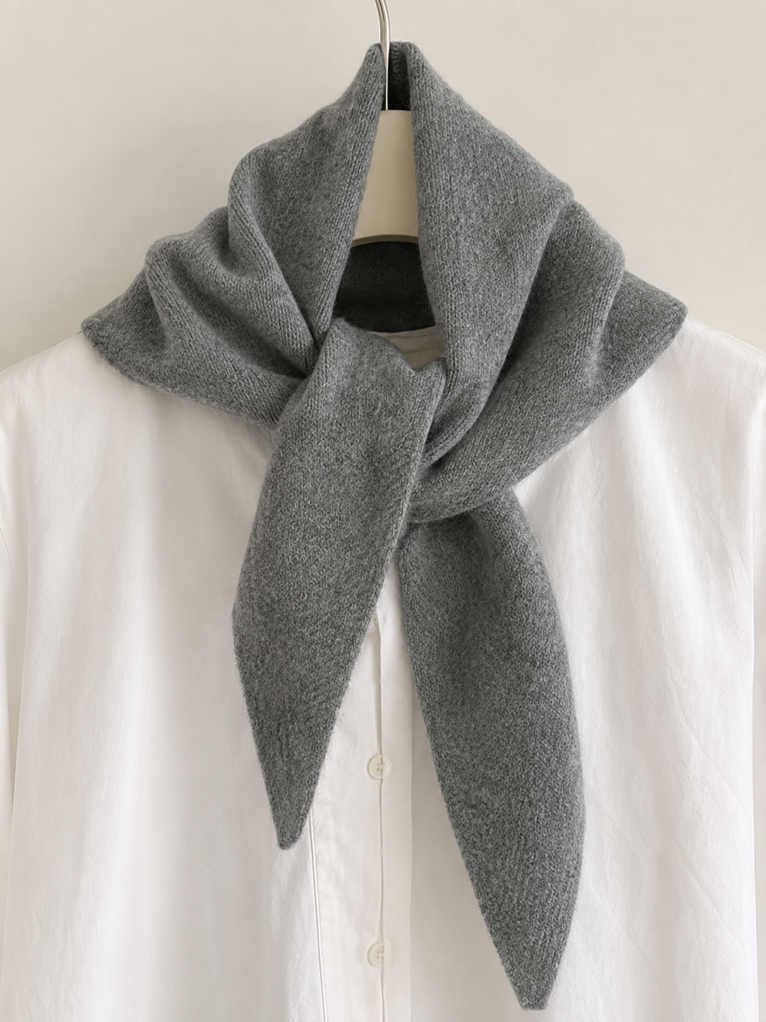 A gray knitted scarf draped over a white button-up shirt on a hanger against a plain light background.