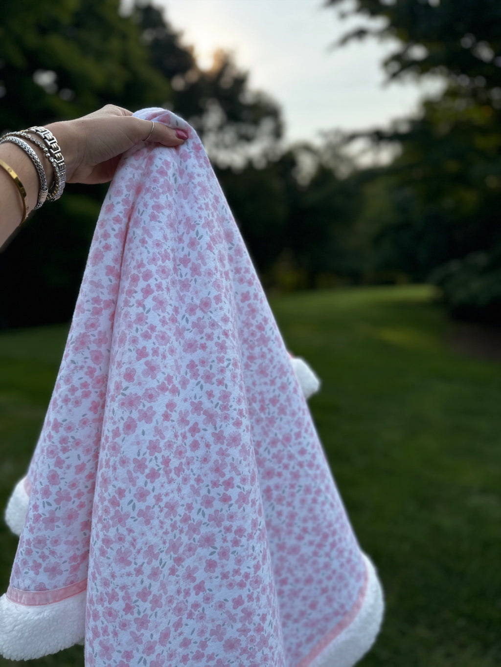 Person holding a pink floral blanket outdoors with greenery in the background