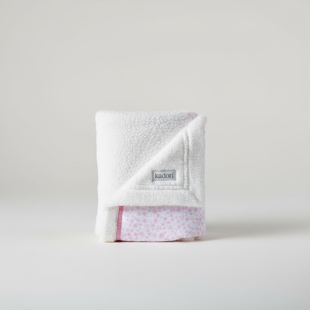 Folded white blanket with a pink border and 'kadori' label on a light gray background